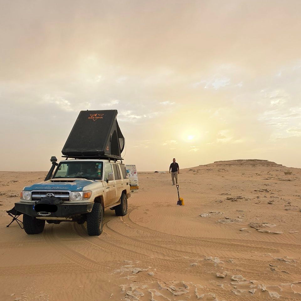 Land Cruiser met opengeklapte hardshell daktent in de woestijn bij zonsondergang